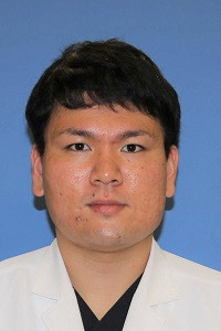 病院助手の林下宗平さんのプロフィール写真。白衣を着て、青い背景の前で微笑んでいる。