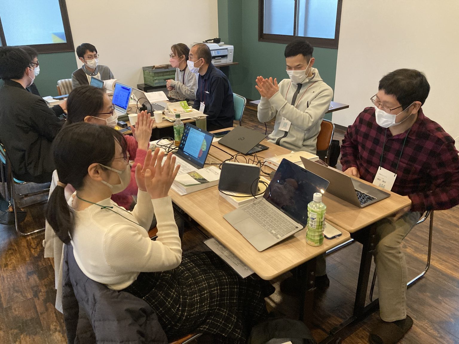 会議室でノートパソコンを使って議論する学生たち。みんなマスクを着用し、テーブルには飲み物が置かれている。