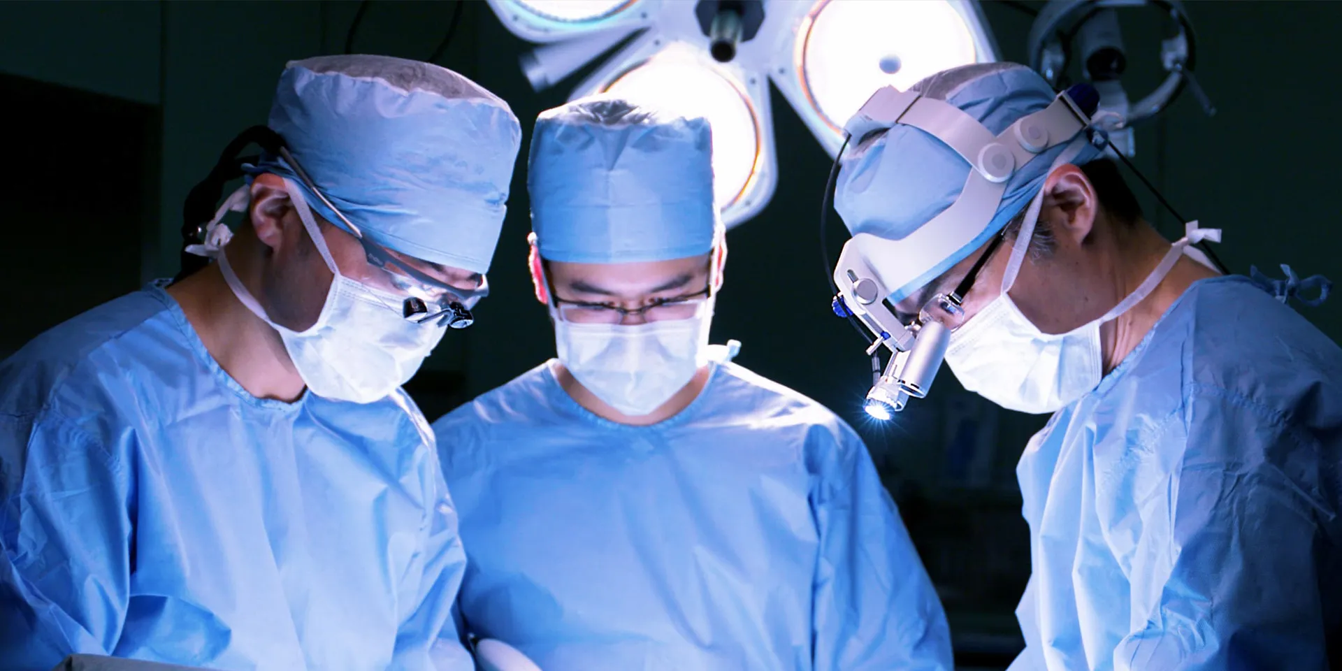 手術室で集中している医師たちが、青い手術着を着用し、患者の治療に取り組んでいる様子。