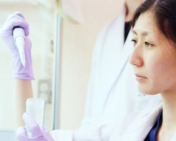 研究室で実験を行う2人の研究者。女性が試薬を扱い、男性がサポートしている様子。