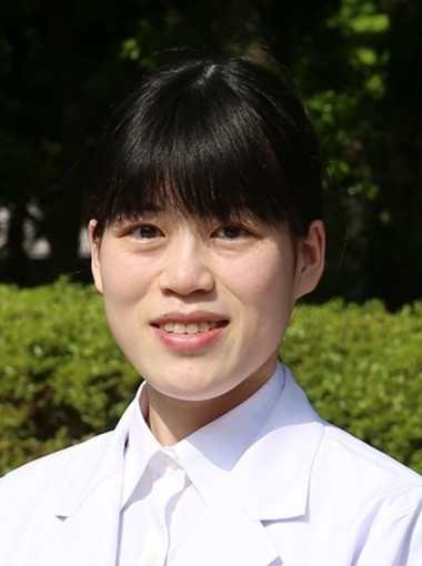 医療白衣を着た男性が、緑の背景の前で微笑んでいる写真。