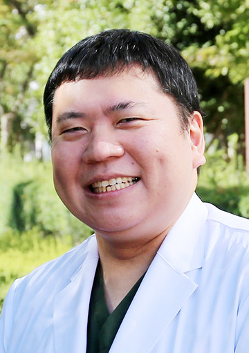 肝胆膵・移植外科学講座の助手、千葉裕仁さんが笑顔で外で撮影された写真。