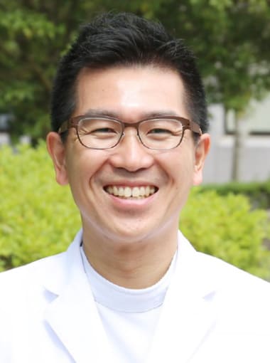 肝胆膵・移植外科学講座の博士研究員、岡田良さんが笑顔でポーズをとる写真。背景には緑の植物が見える。