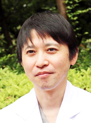 医療白衣を着た男性が、緑の背景の前で微笑んでいる写真。