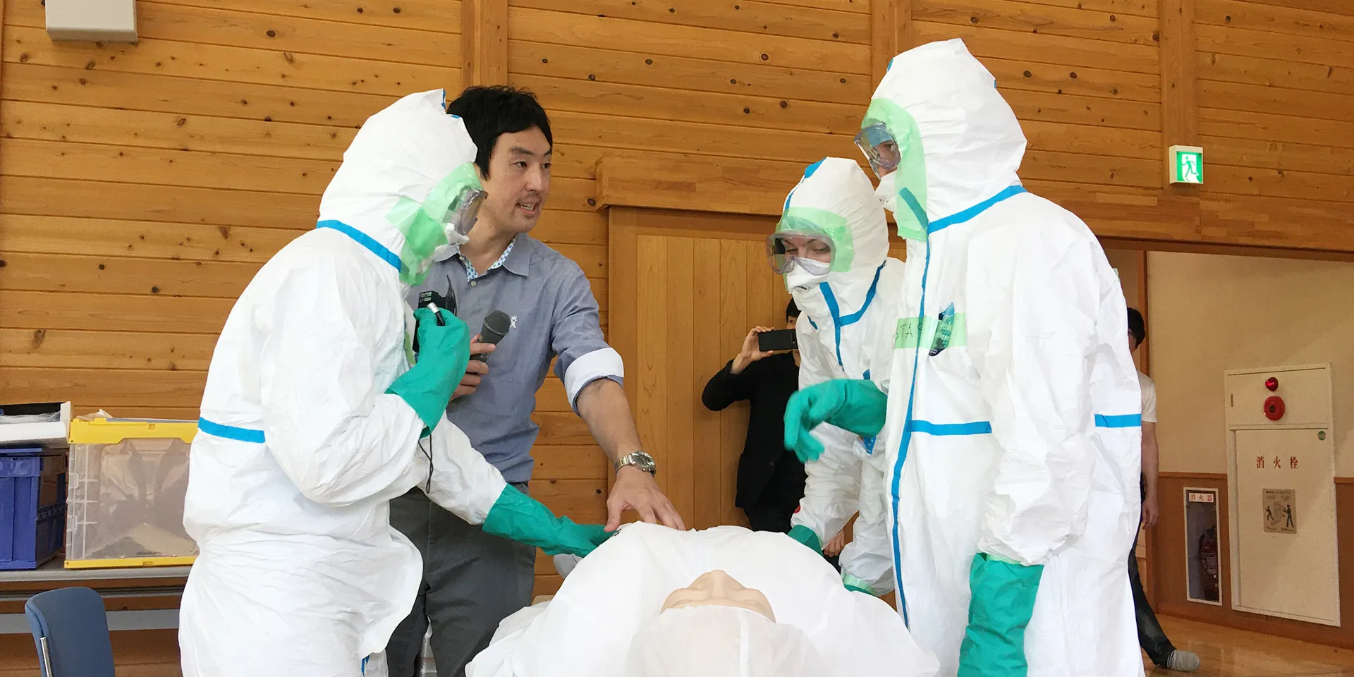 放射線災害医療の訓練を受ける医療従事者たちが、模擬患者に対して手技を行っている様子。