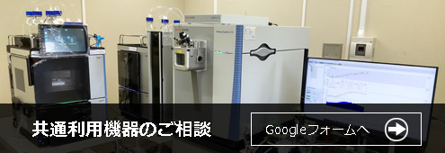 高精度な質量分析計システムとデータ解析用モニターが設置された研究室の画像。