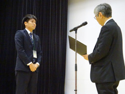 受賞式で表彰される学生が、壇上でスピーチを聞いている様子。