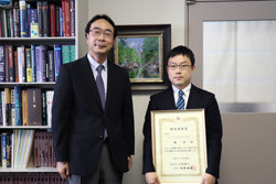 林先生が2020年度日本肝臓学会研究奨励賞を受賞し、賞状を持っている写真。背景には本棚が見える。