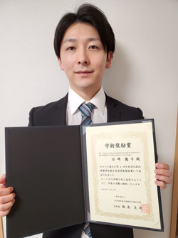 受賞した学生が学位証明書を持って微笑んでいる写真。