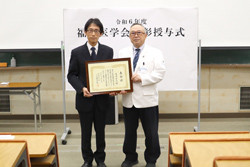 福島県立医科大学での受賞式の様子。受賞者が表彰状を持ち、教授と共にポーズを取っている。