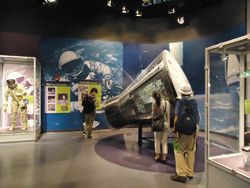 宇宙関連の展示室で、宇宙服を着た人々や宇宙船の模型を見学している様子。
