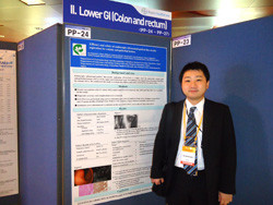 福島県立医科大学の研究発表ポスターの前に立つ男性。ポスターには「Lower GI (Colon and rectum)」と題された内容が記載されている。