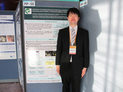 福島県立医科大学の研究発表会で、スーツを着た男性がポスターの前に立っている様子。
