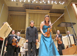 ボストン交響楽団の演奏後、観客に向かってお辞儀をする演奏者たちの姿。女性は青いドレスを着てバイオリンを持っている。