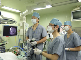 医療現場で手術を行う医師たちが、モニターを見ながら真剣に作業している様子。