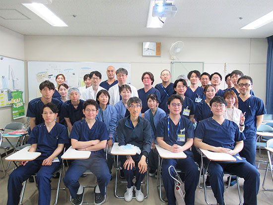 医療従事者たちが集まるカンファレンスの様子。手術着を着た医師や看護師が笑顔でポーズをとっている。