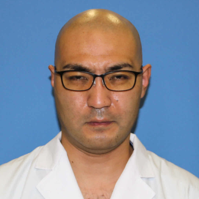 医学部麻酔科学講座の助手、小川琢也さんのプロフィール写真。白衣を着て、眼鏡をかけた男性が青い背景の前で真剣な表情をしています。