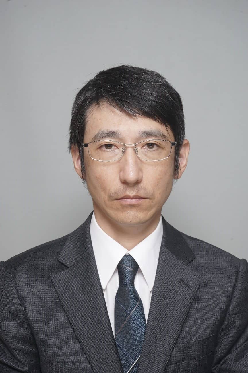 教授の立石善隆氏がスーツを着て正面を向いているポートレート。背景は無地でシンプル。