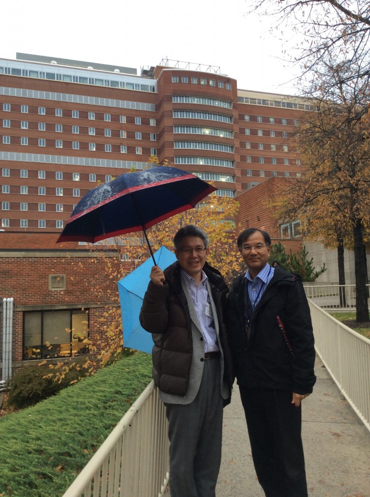NIHの恩田先生と建物前で傘を持って立っている様子。