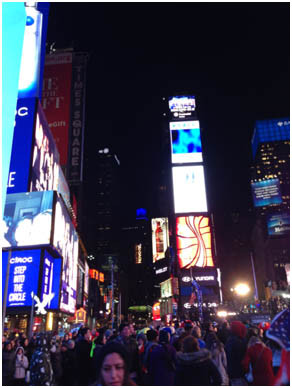 夜のタイムズスクエアに集まる多くの人々と、明るく輝くネオンサインや広告が並ぶ光景。