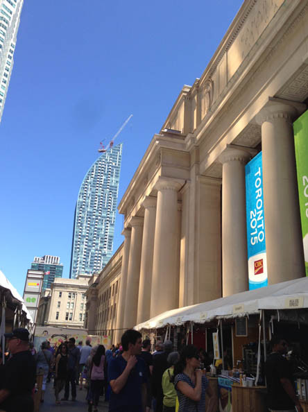 大きな柱が特徴的な建物の前でイベントが開催され、多くの人々が歩いている。