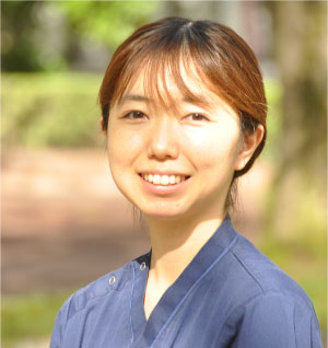 大学院生の赤沼春菜さんが笑顔でポーズをとっている写真。背景には緑の木々が見える。