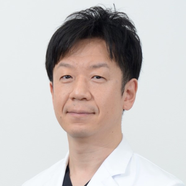 准教授の志賀哲也氏のポートレート。白衣を着て微笑む姿が印象的。