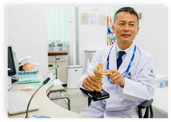 医師が脊椎模型を手に持ちながら微笑んでいる診察室の様子。