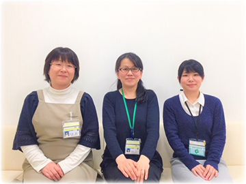 院内がん登録室のスタッフ3名が並んで座っている写真。各自が名札をつけており、明るい背景の前で微笑んでいる。