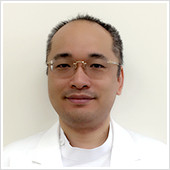 腫瘍内科医の佐々木栄作さんが白衣を着て微笑んでいるポートレート。