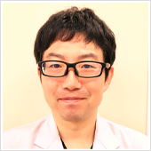 腫瘍内科医の名取穣博士が白衣を着て微笑んでいるポートレート。