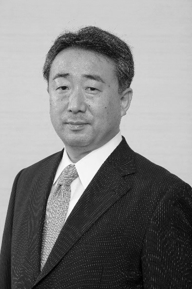 四代飯田知弘氏のポートレート。ビジネススーツを着用し、真剣な表情でカメラを見つめている。
