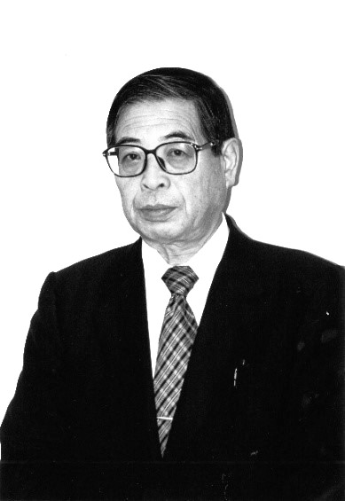 三代加藤桂一郎氏のスーツ姿のポートレート。眼鏡をかけ、真剣な表情でカメラを見つめている。