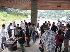 BBQ大会で楽しむ参加者たちが集まり、食材を焼いている様子。