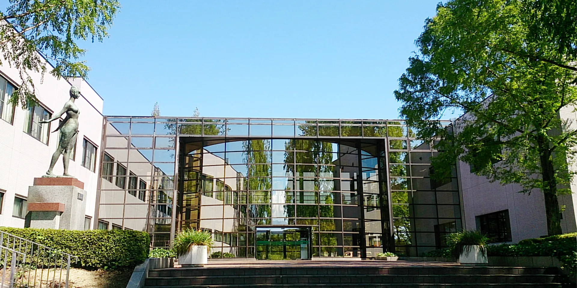 福島県立医科大学のキャンパス入口に立つ彫刻とガラス張りの建物の風景。