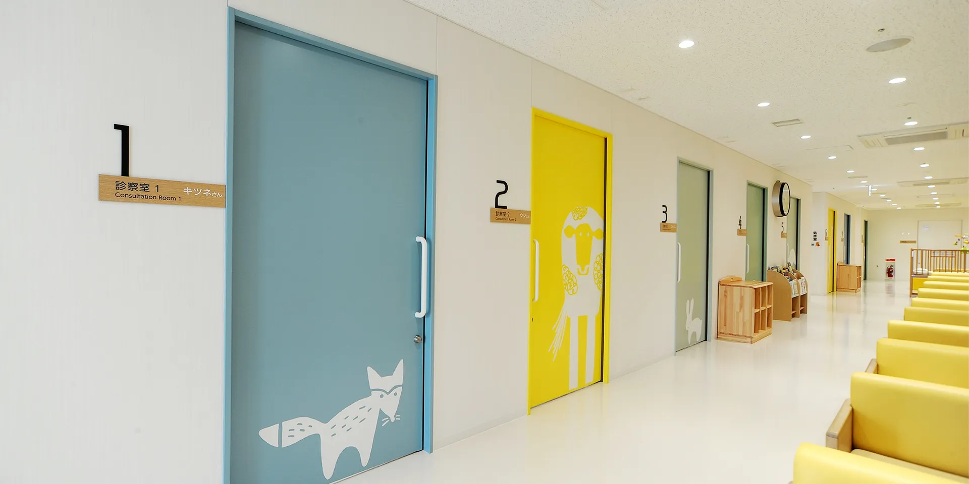 診察室のドアが並ぶ明るい待合室の風景。各部屋には動物のイラストが描かれている。