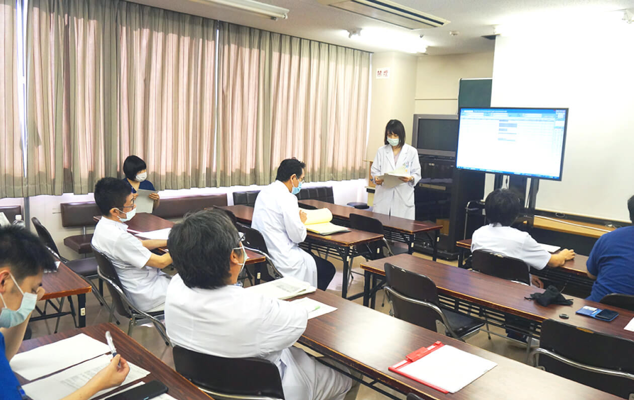 医学生が研修室でプレゼンテーションを行い、他の医学生が聴講している様子。