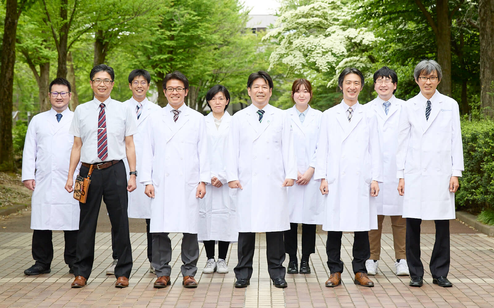 福島県立医科大学のスタッフが白衣を着て並んでいる写真。緑豊かな公園での集合写真。