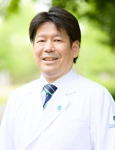 主任教授の鈴木義行氏が白衣を着て微笑んでいるポートレート。背景には緑の木々が見える。