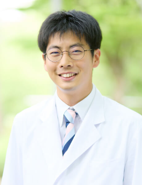 会津中央病院の放射線科医員、梅宮和真さんが白衣を着て微笑んでいる写真。背景には緑の自然が広がる。