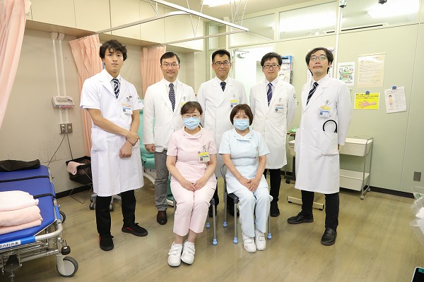 医療スタッフが病院の一室で集合写真を撮影。白衣を着た医師と看護師が並んで立っている。