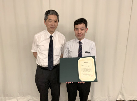 鈴木英二先生が福島県立医科大学医学部同窓会地域学術振興賞を受賞し、賞状を持って笑顔でポーズをとる写真。