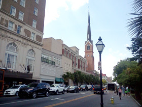 街並みと高い教会の尖塔が見える風景、車が行き交う通りの様子。