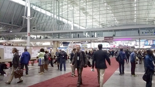 国際学会のポスターセッション会場で、多くの参加者が交流している様子。