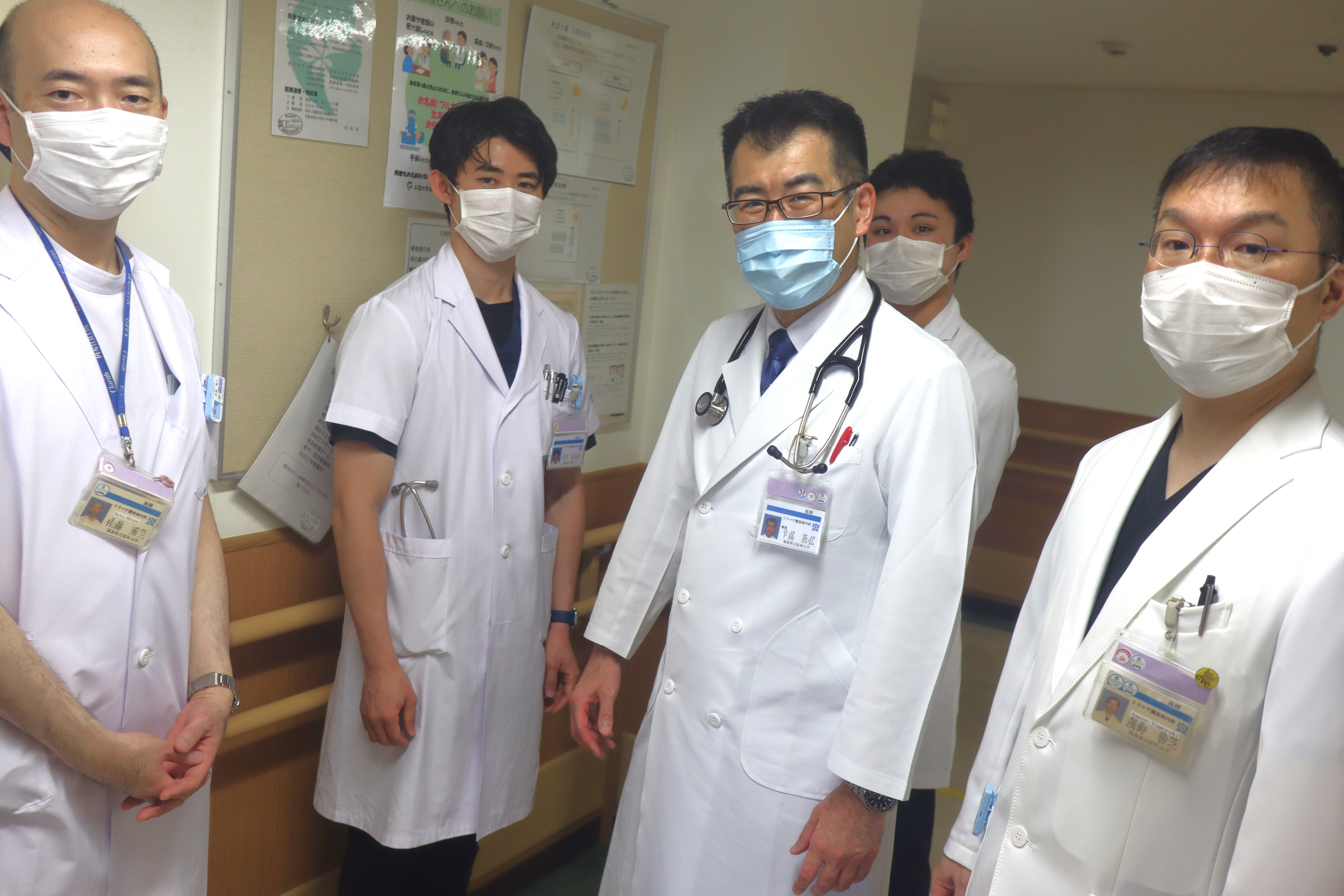 医療スタッフが病院の一室で集合写真を撮影。白衣を着た医師と看護師が並んで立っている。