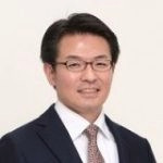 教授の田巻倫明がスーツを着て微笑んでいるポートレート。背景はシンプルな白。