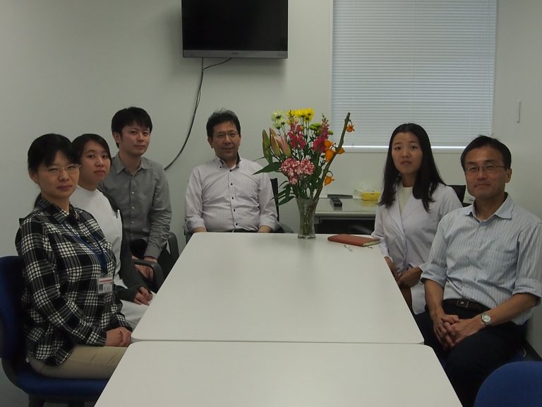福島県立医科大学の教育活動に参加する6人の学生と教員が、花を飾ったテーブルの前で笑顔で座っている様子。