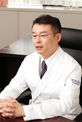 白衣を着た小島が話をしている様子