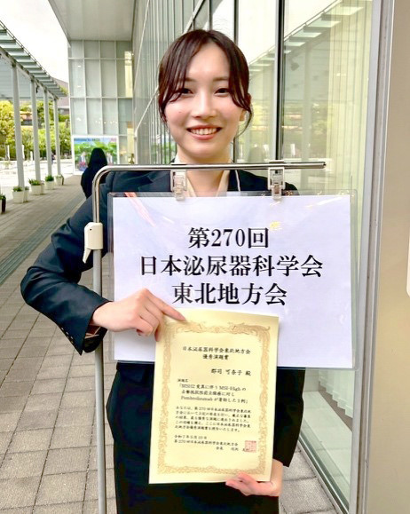 日本泌尿器科学会東北地方会で賞状を持って立つ女性。