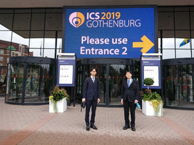 スーツ姿の2人が「ICS 2019 GOTHENBURG」の看板前に立っている。